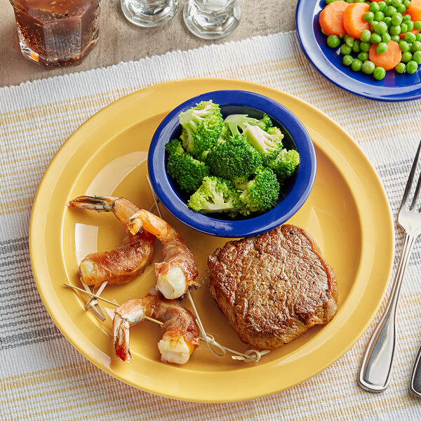 A plate of food with shrimp, broccoli, peas, and carrots on an Acopa yellow melamine plate with a fork and knife.