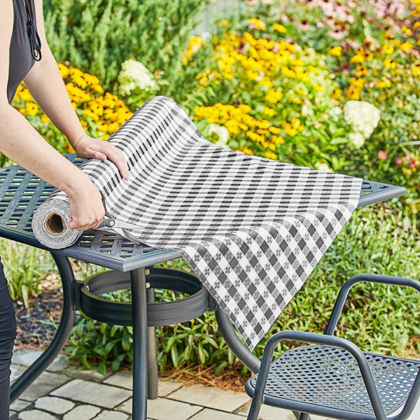 A woman rolling a black checkered vinyl table cover onto a table.