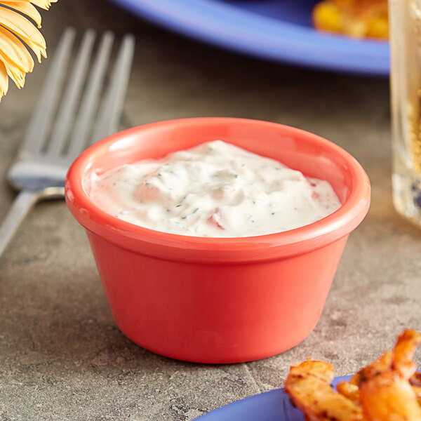 An Acopa Foundations orange melamine ramekin filled with white sauce on a table.
