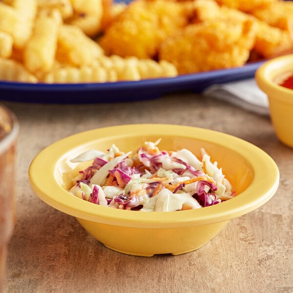 A yellow Acopa Foundations melamine bowl of coleslaw and chicken nuggets on a table.
