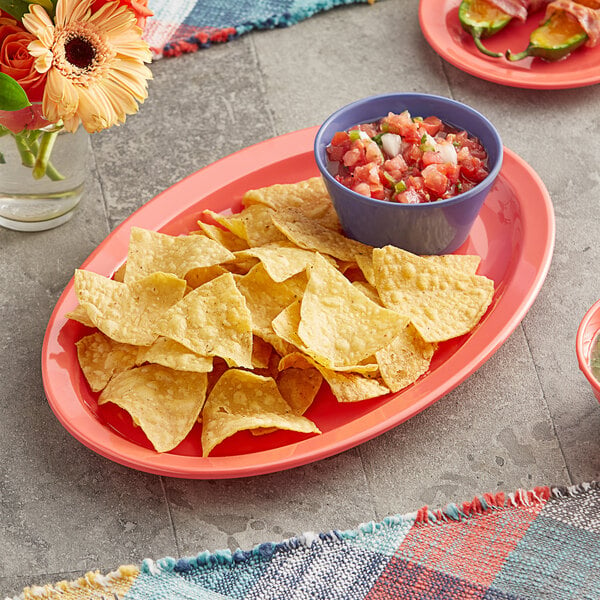 An Acopa orange melamine oval platter with a bowl of salsa and a plate of chips on a table.