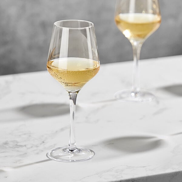 Two Della Luce white wine glasses on a marble table.