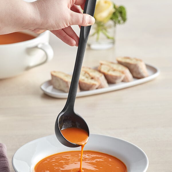 A person using a Tablecraft black silicone-coated stainless steel ladle to pour soup into a bowl.