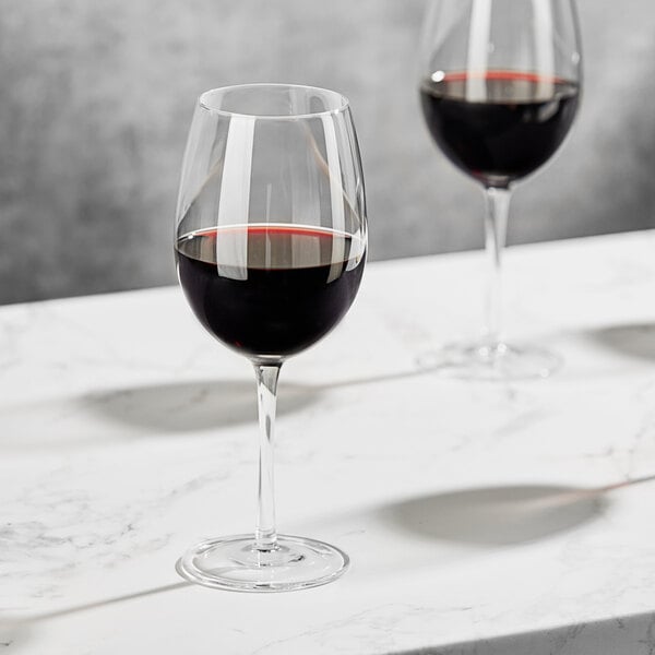 Two Della Luce Maia all-purpose wine glasses filled with red wine on a marble table.