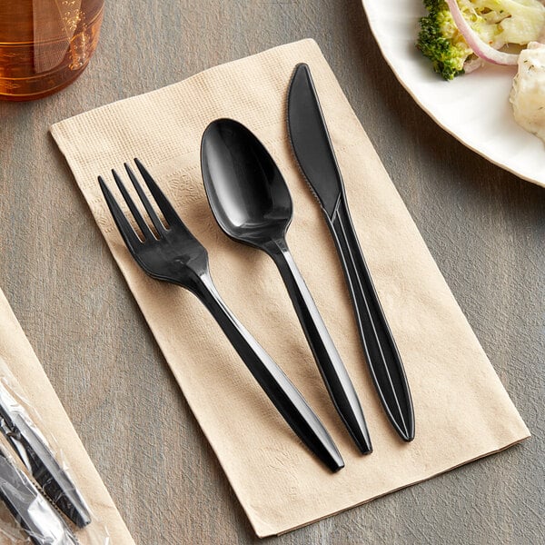 A black plastic Choice spoon and fork on a napkin next to a plate with broccoli.
