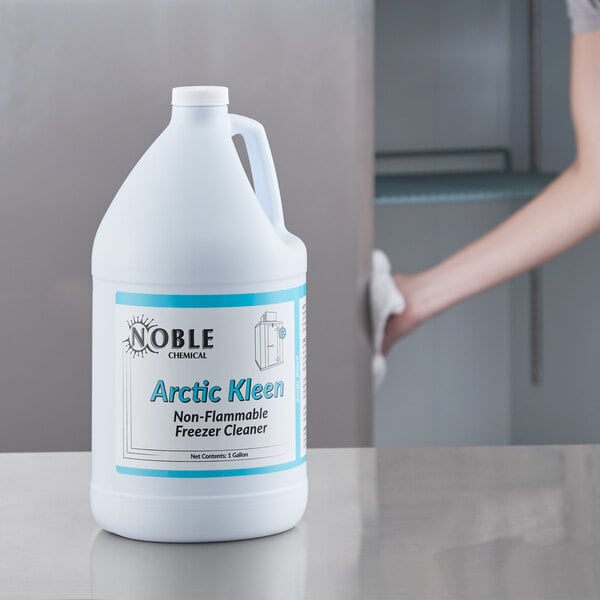A woman holding a white jug of Noble Chemical Arctic Kleen Freezer Cleaner with a blue label.