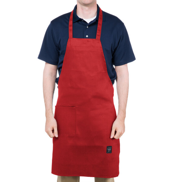A man wearing a red Chef Revival bib apron with one pocket.