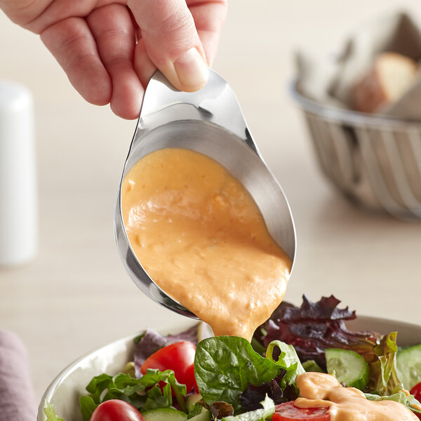 A person using a Vollrath stainless steel ramekin with a handle to pour sauce over a salad.