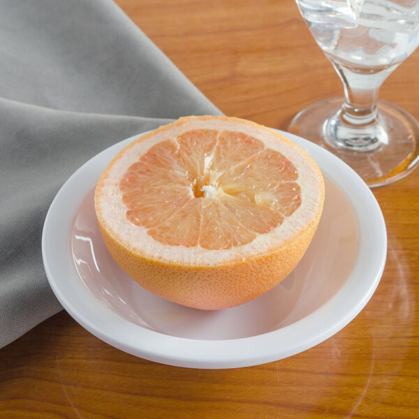 A Carlisle white melamine grapefruit bowl filled with half of a grapefruit next to a glass of water on a table.