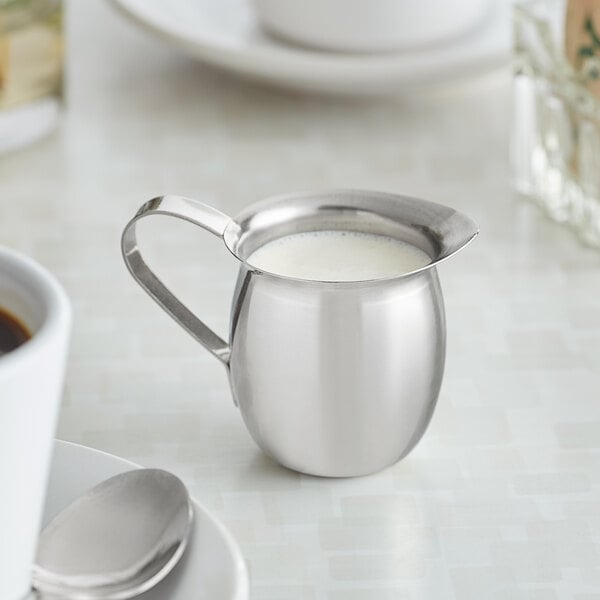 A Vollrath stainless steel bell creamer with milk.