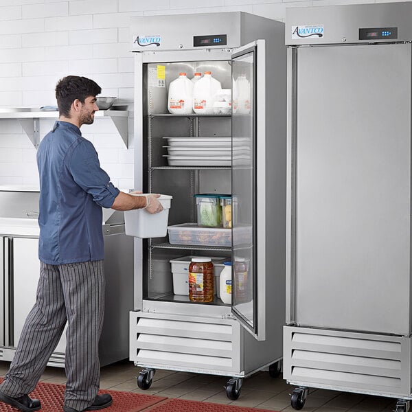 A man opening a stainless steel solid door reach-in refrigerator in a professional kitchen.
