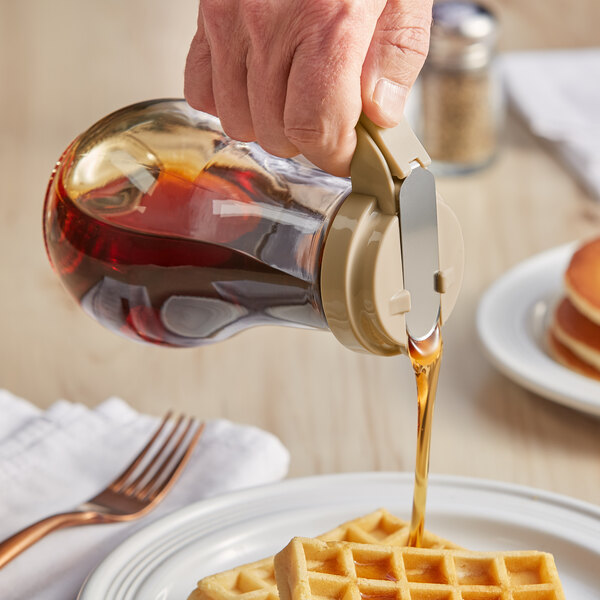 A hand using a Vollrath glass syrup dispenser to pour syrup on waffles.