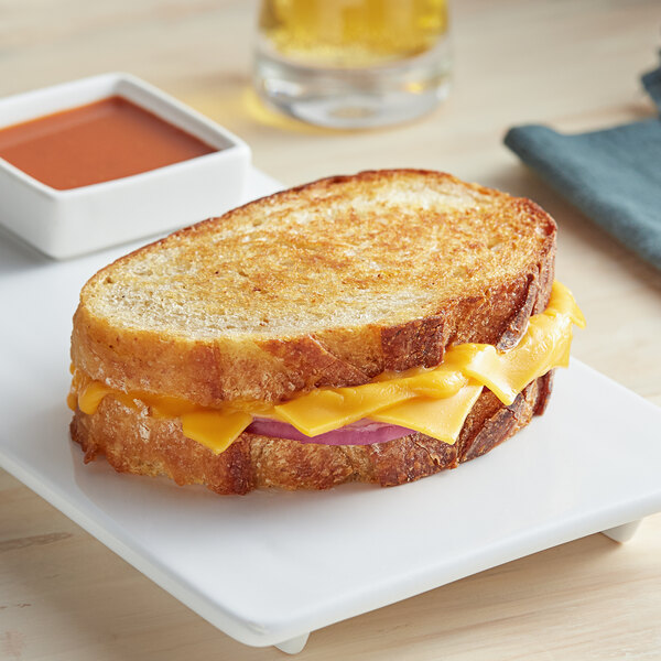 A grilled cheese sandwich made with GOOD PLANeT plant-based vegan cheddar cheese slices on a plate with a bowl of red sauce.