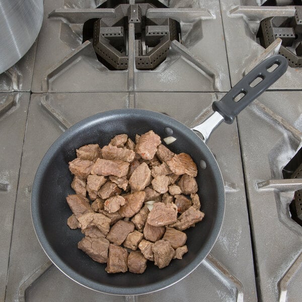 A Vollrath stainless steel non-stick fry pan filled with meat cooking on a stove.