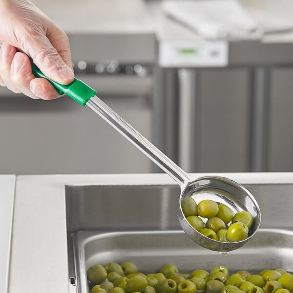A hand holding a Choice green perforated portion spoon filled with green olives.