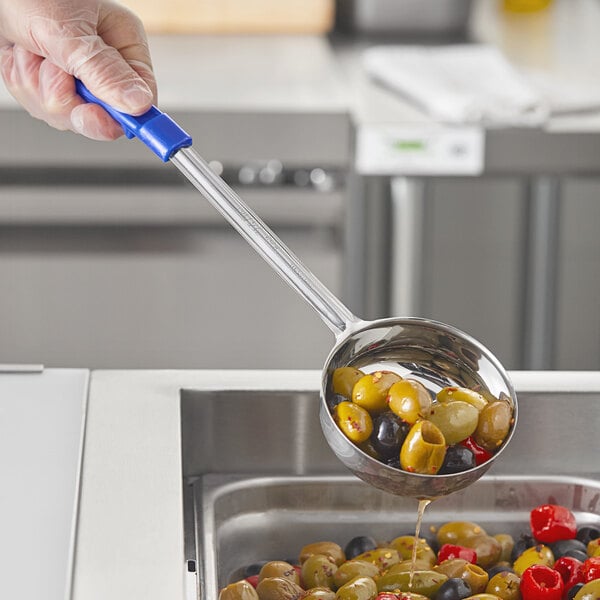 A person in a glove using a blue Choice perforated portion spoon to serve olives.