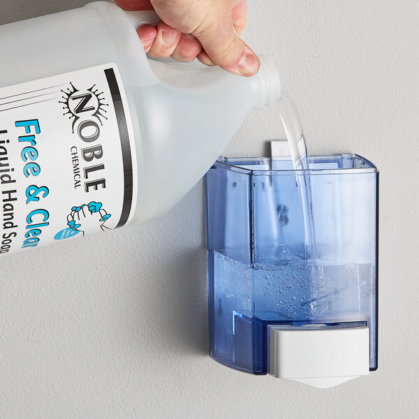 A hand pouring Noble Chemical Free & Clear liquid hand soap into a dispenser.