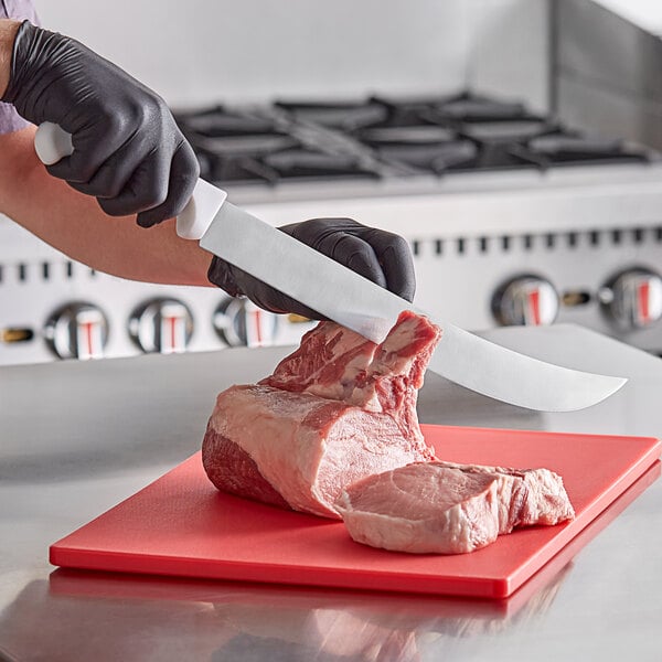 A person in gloves using a Choice cimeter knife to cut meat on a cutting board.