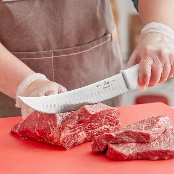 A person using a Choice cimeter knife to cut meat on a red cutting board.