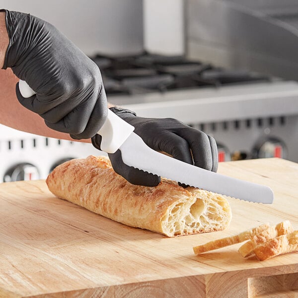 A person in black gloves using a Choice serrated bread knife to cut bread on a cutting board.