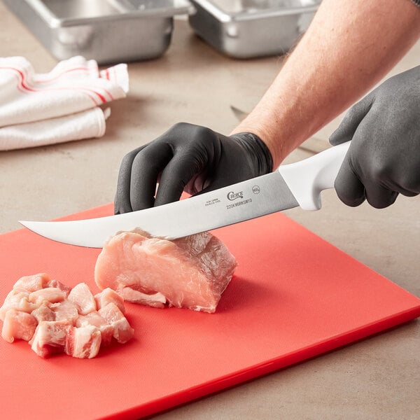 A person using a Choice 10" Breaking Knife to cut meat on a red cutting board.