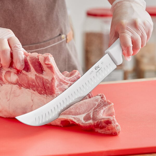 A person using a Choice cimeter knife to cut meat on a counter.
