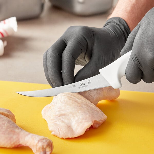 A person in gloves using a Choice curved boning knife to cut chicken.
