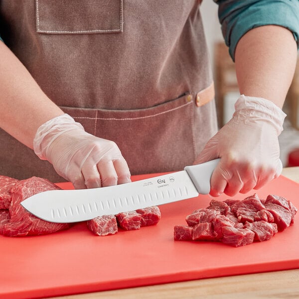 A person using a Choice 10" Granton Edge Butcher Knife to cut raw meat on a cutting board.