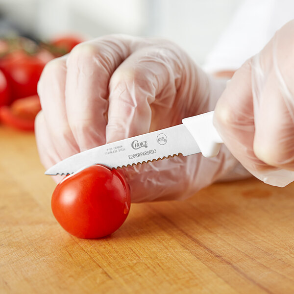A person in gloves uses a Choice serrated edge paring knife to cut a tomato.