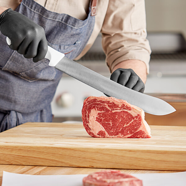 A person cutting meat with a Choice 12" Butcher Knife on a wooden cutting board.