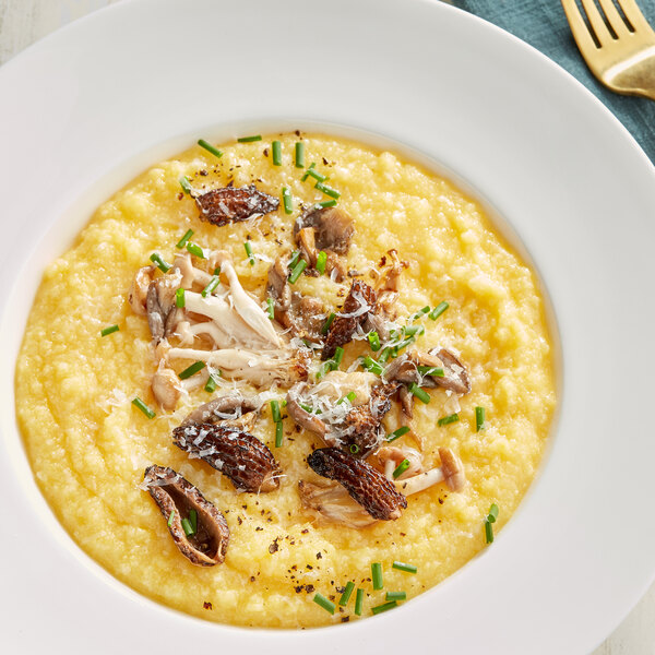 A white bowl of creamy polenta with mushrooms and a fork.