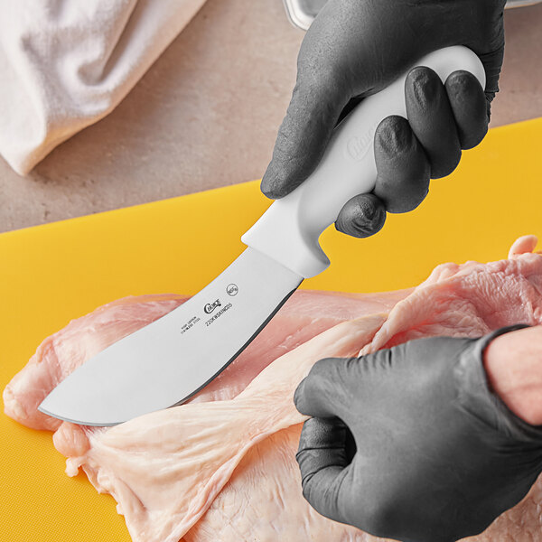 A person in gloves using a Choice curved skinning knife with a white handle to cut meat.