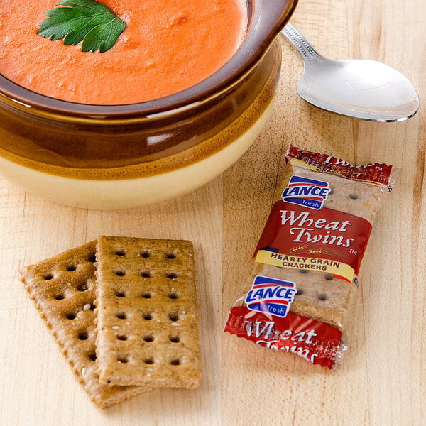 A bowl of soup next to a package of Lance Wheat Twins crackers and a spoon.