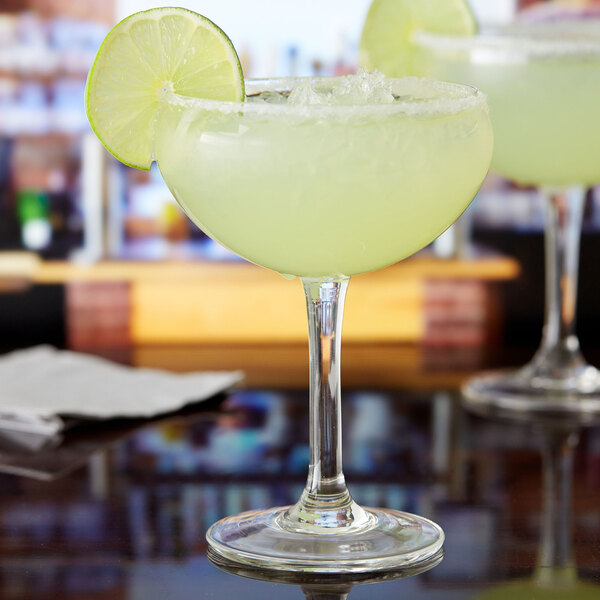 Two margarita glasses with lime wedges and drinks on a bar.