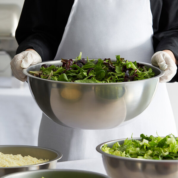 A person holding a Vollrath heavy duty stainless steel mixing bowl full of salad.