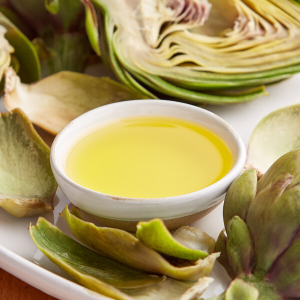 A bowl of clarified butter next to artichokes.