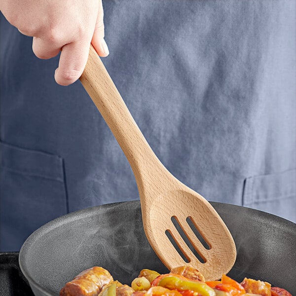 A person stirring a pan with an OXO wooden slotted spoon.