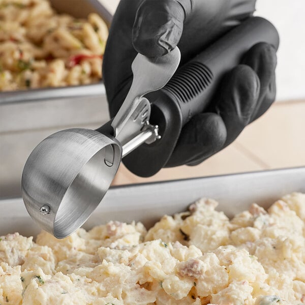 A person using an OXO Good Grips black thumb press scoop to serve food