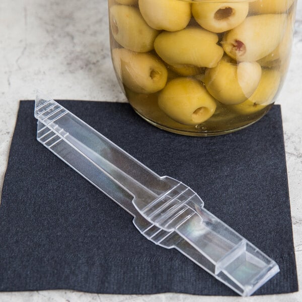 A plastic tong with a clear plastic handle next to a bowl of green olives.