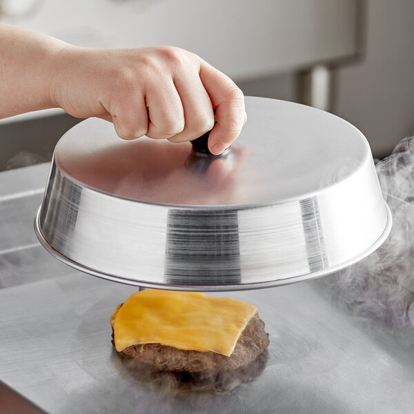 A person holding an American Metalcraft aluminum basting cover over a hamburger.