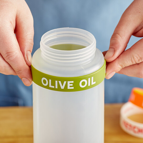 A person holding a plastic bottle of olive oil with a green label.