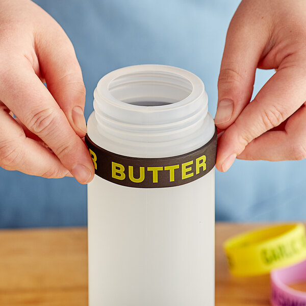 A person's hands holding a white container with a black band that says "Butter" on it.