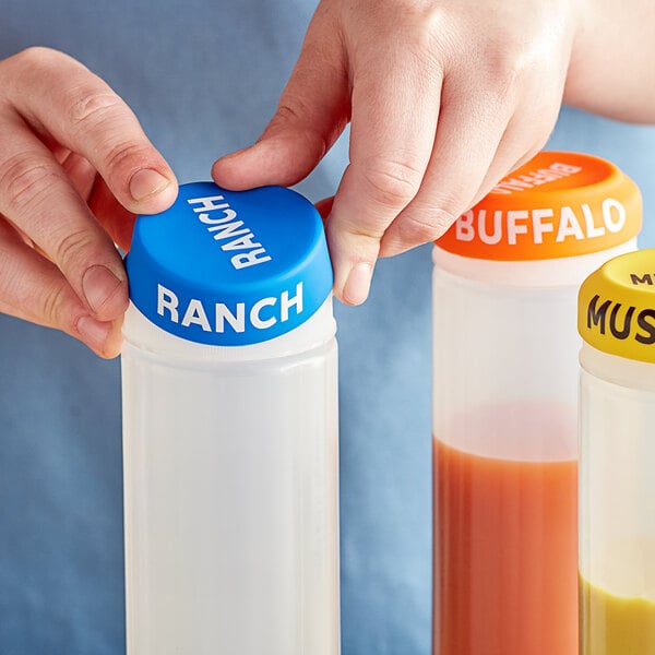 A hand holding a bottle of ranch with an orange and blue lid.