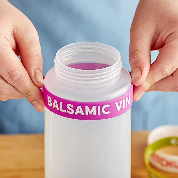 A person holding a plastic bottle of balsamic vinegar with a pink label band on it.