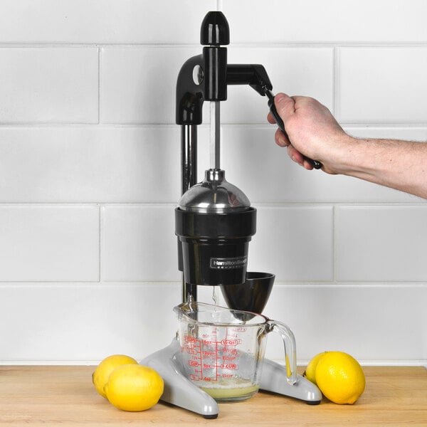 A hand using a Hamilton Beach citrus juicer to squeeze lemons on a counter.