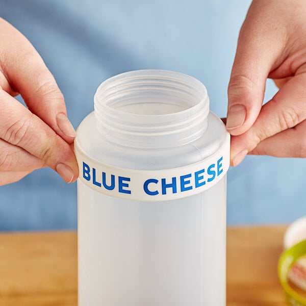 A person using a blue silicone band to label a plastic squeeze bottle of blue cheese.