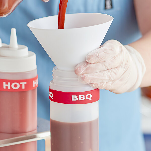 A hand pouring red sauce into a white squeeze bottle with a white Choice BBQ label band.