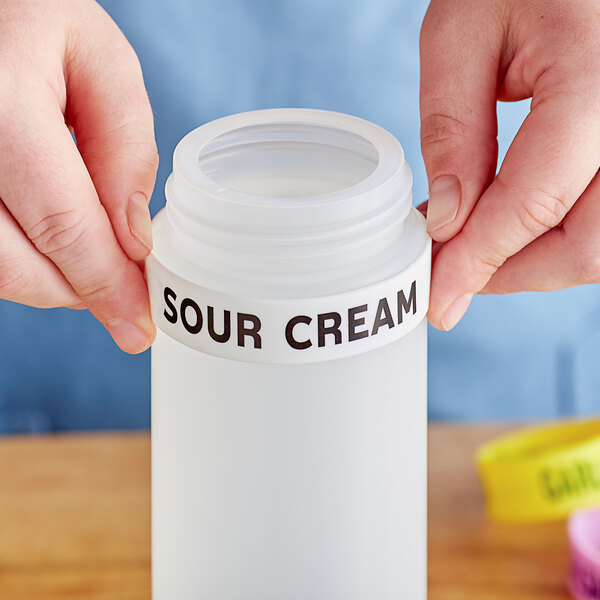 A person holding a white squeeze bottle with a yellow label band reading "Sour Cream"