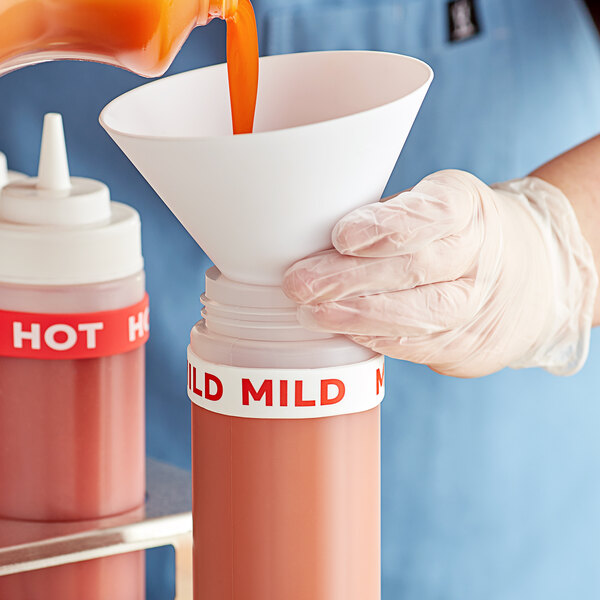A hand using a funnel to pour liquid into a squeeze bottle with a "Mild" silicone label band.