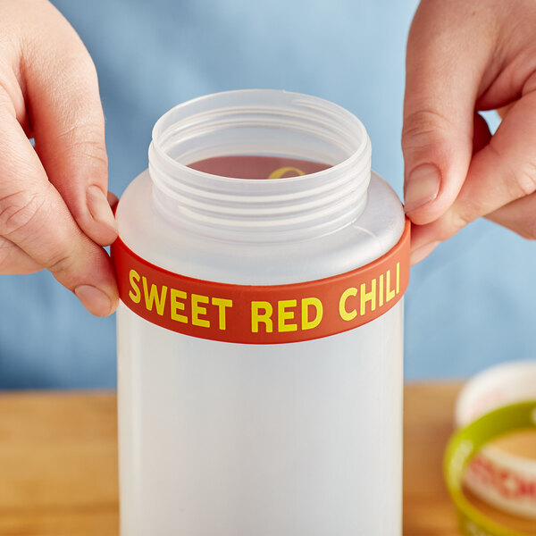 A person holding a plastic container with a red Sweet Red Chili label band around the lid.